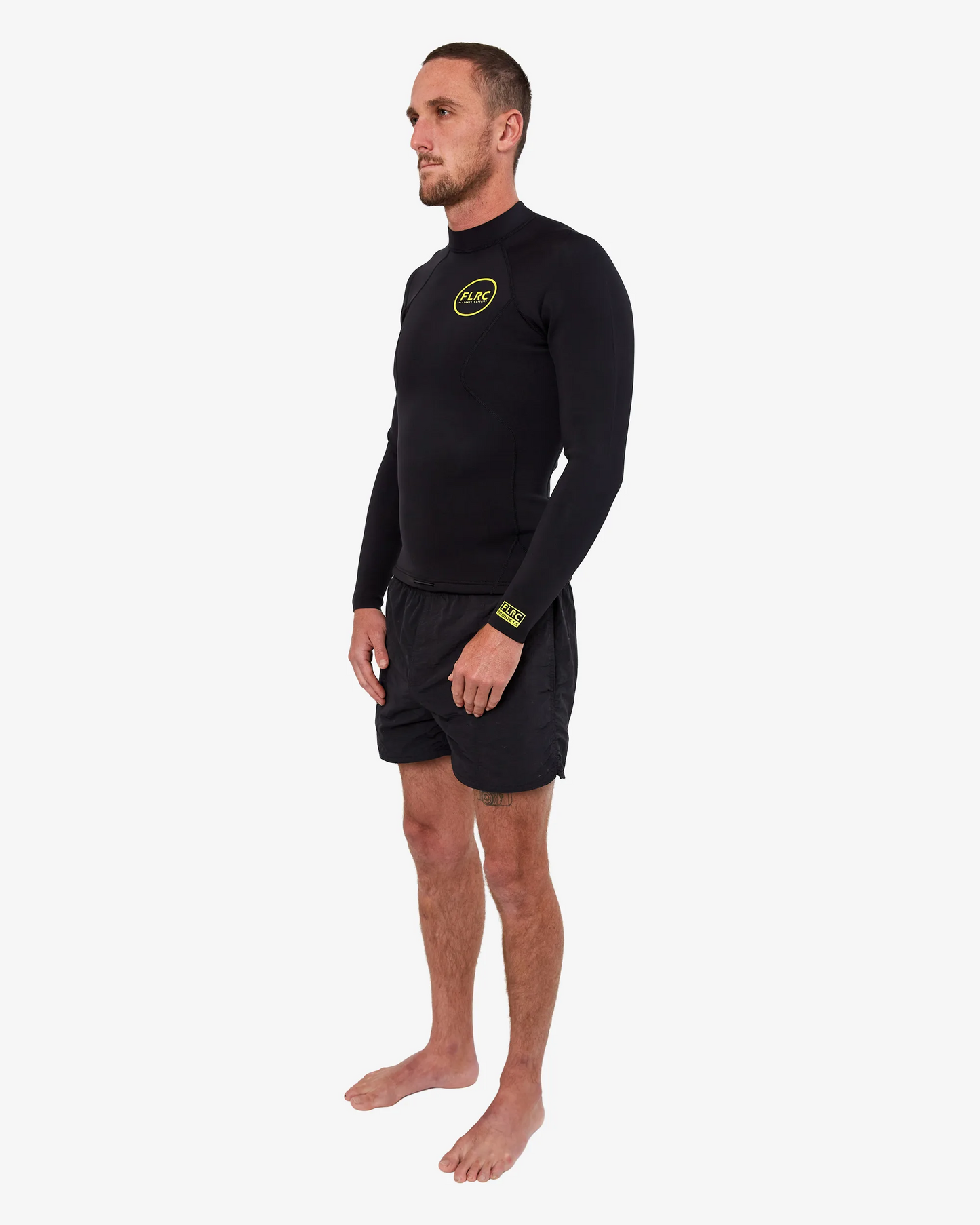 Man wearing black FLRC 1.5mm wetsuit top with yellow logo, angled view in studio.