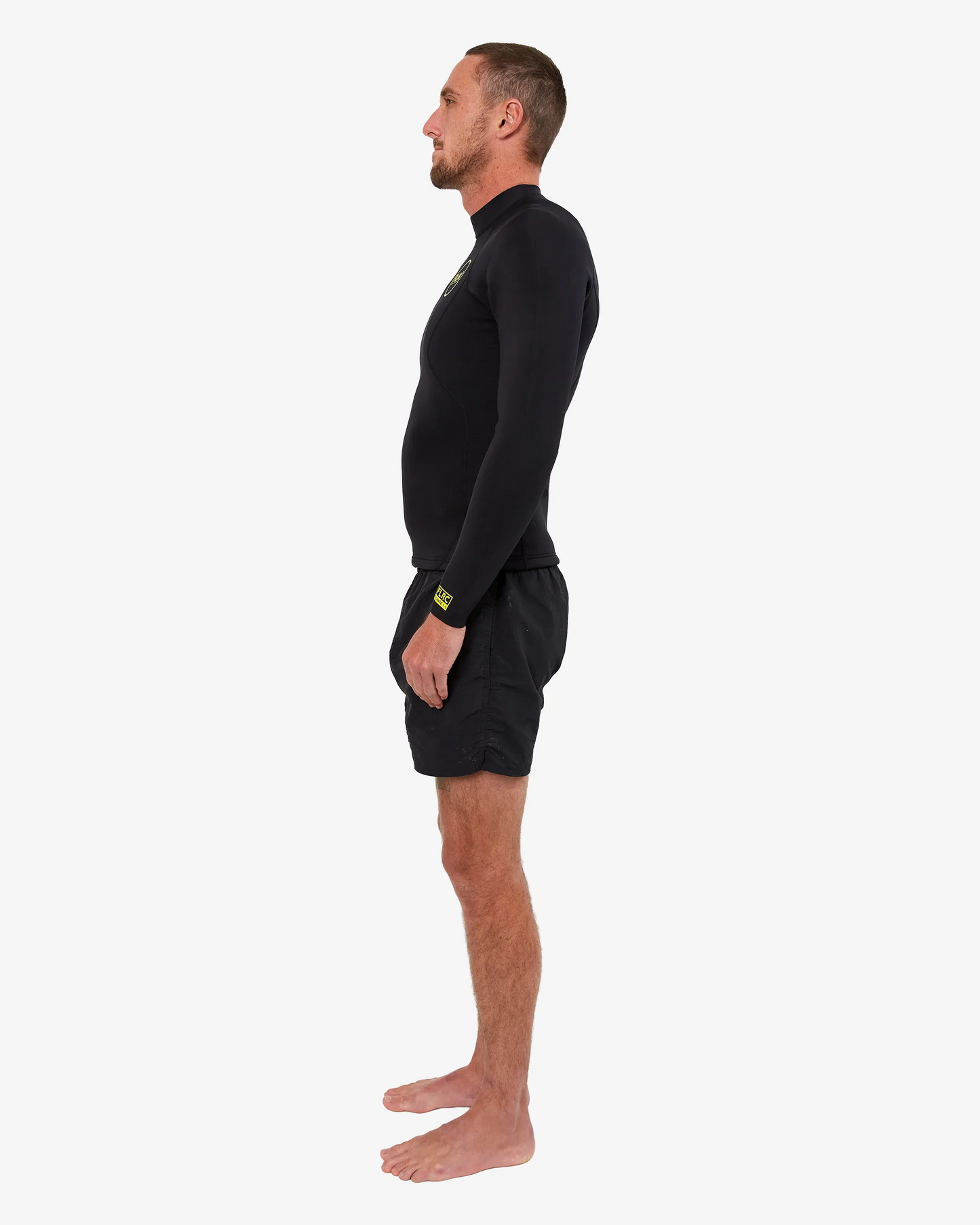 Man wearing black FLRC 1.5mm wetsuit top with yellow logo, side view in studio.