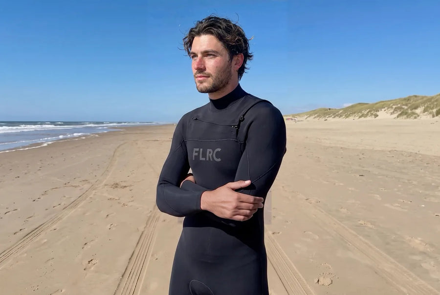 Surfer standing on an empty beach in the Men's 3/2mm Steamer V3, arms folded, looking out to sea under a clear sky