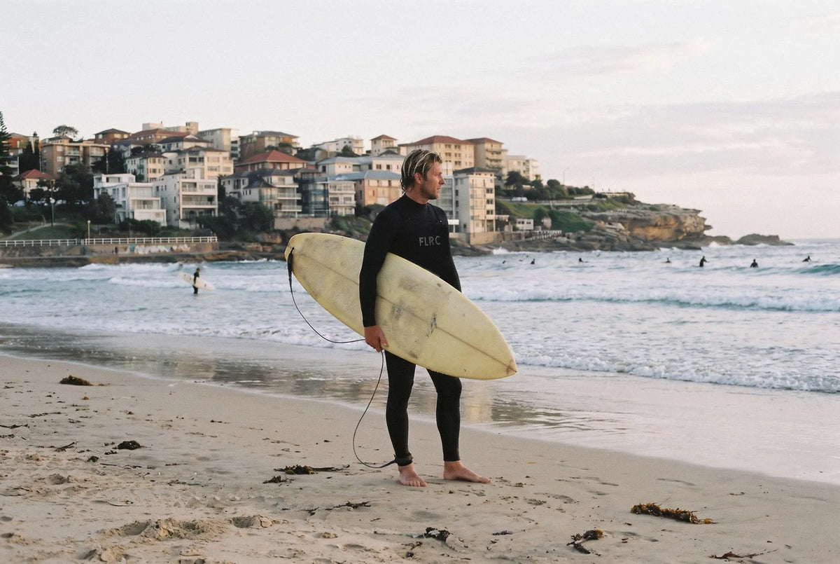 Surfer in a Flatrock steamer holding a board at the water's edge, Bondi on an overcast morning