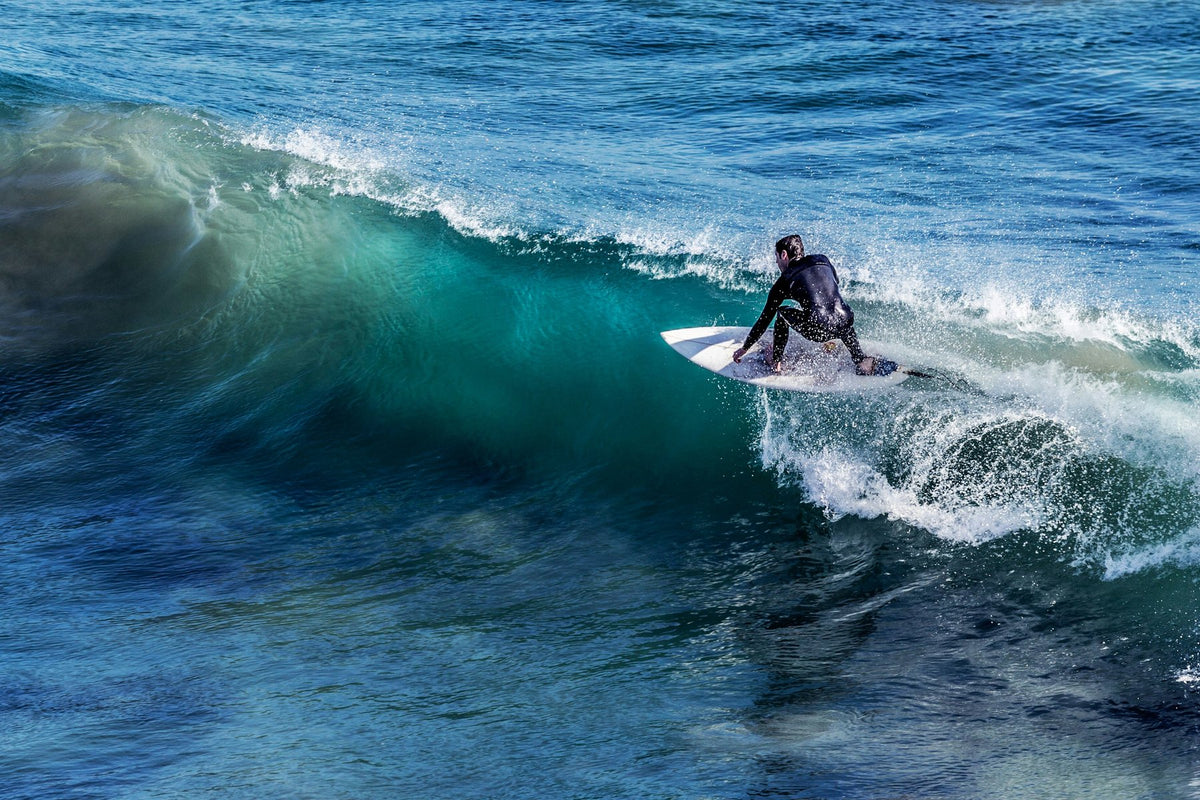Surfer in a full wetsuit riding a shortboard across a clean blue wave