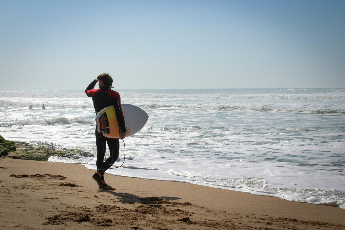 Surfer in a full wetsuit walking along the beach to the water with his board