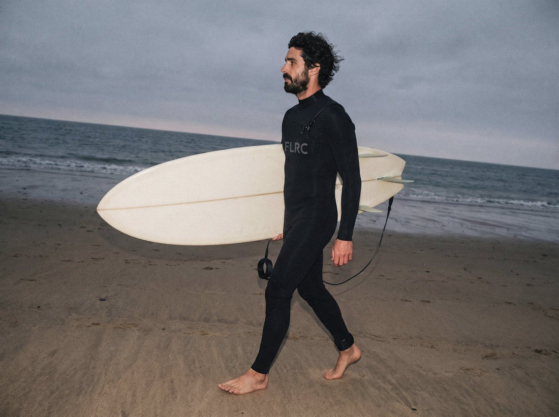 Surfer walking and carrying a surfboard in the Flatrock Surf Sarvo Series III wetsuit on the beach