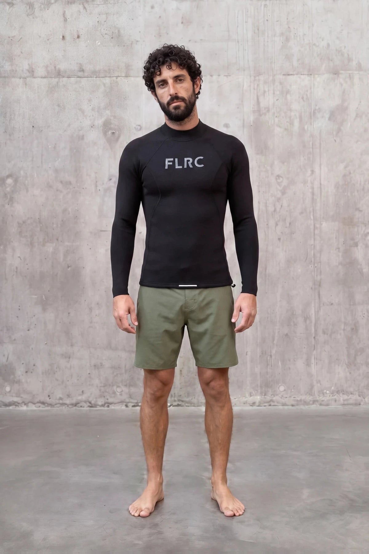 Man in Men's 1.5mm Wetsuit Top V2 with grey FLRC chest logo, front view against a concrete wall