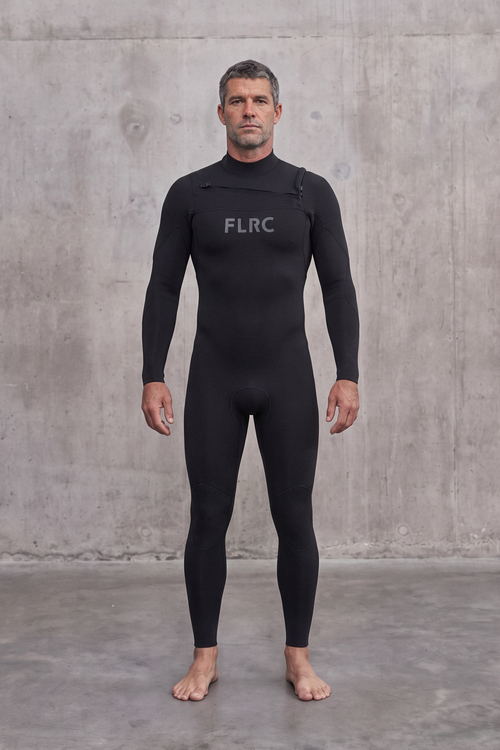 Man in Men's 3/2mm Fullsuit V3 wetsuit, front view with grey FLRC chest logo against a concrete wall