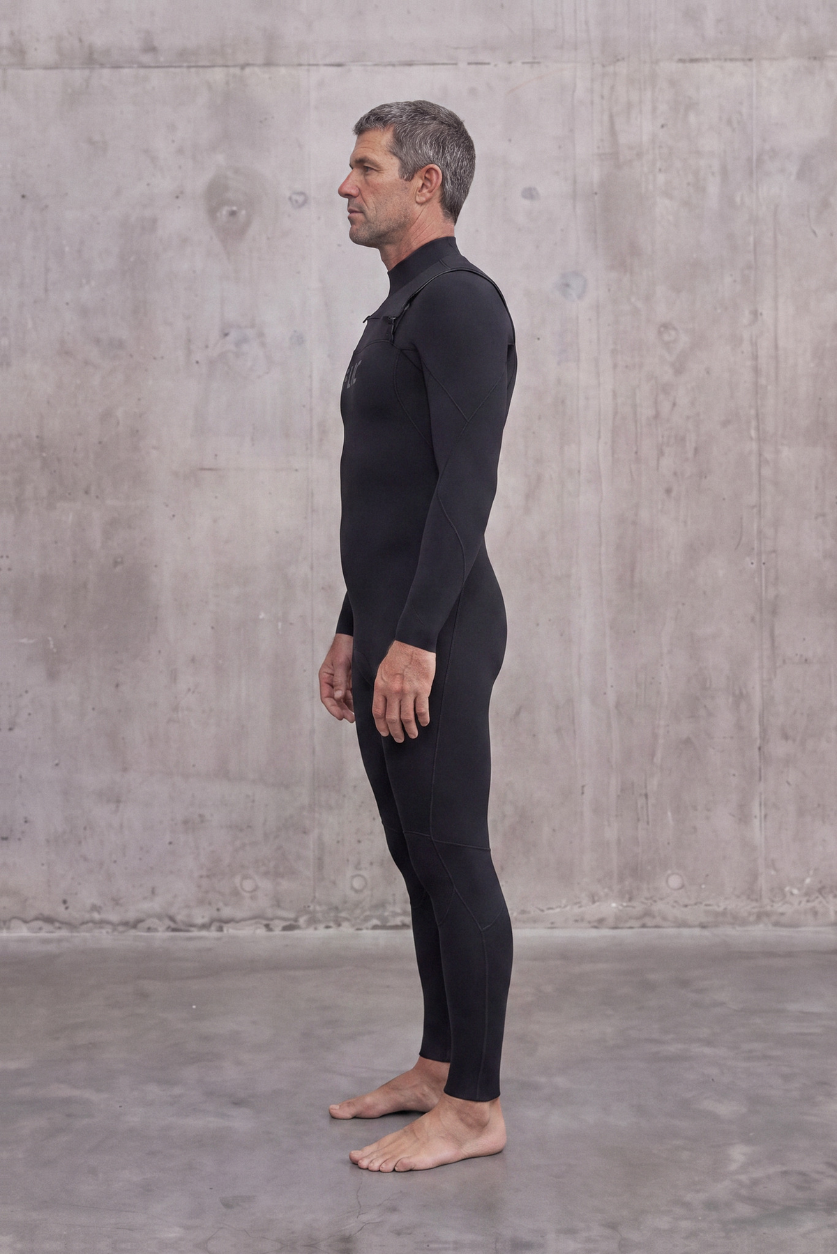 Side view of a man in the Men's 3/2mm Fullsuit V3 wetsuit, standing barefoot on concrete