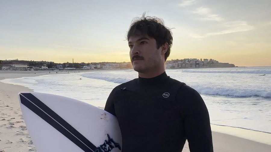 Surfer carrying a board along Bondi at sunrise in the Men's 3/2mm Steamer V2