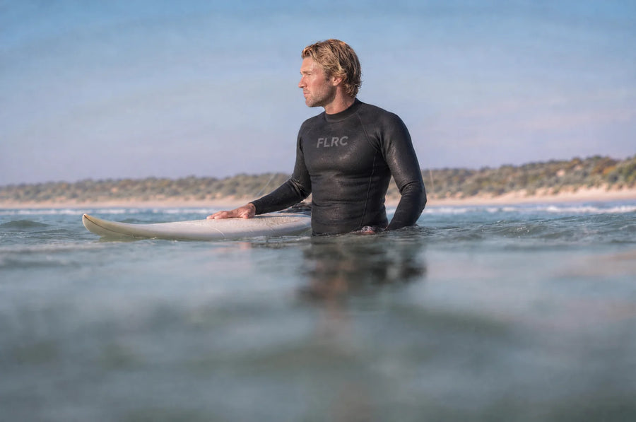 Surfer sitting on a longboard in the Men's 1.5mm Wetsuit Top V2, a long Australian beach and low dunes behind him