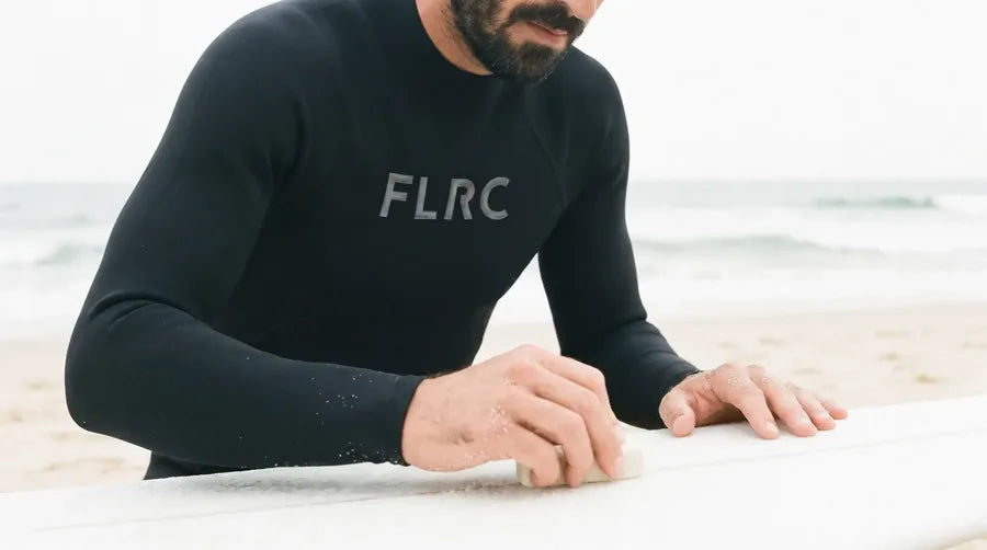 Close crop of the Men's 1.5mm Wetsuit Top V2, hands resting on a surfboard rail at the shoreline